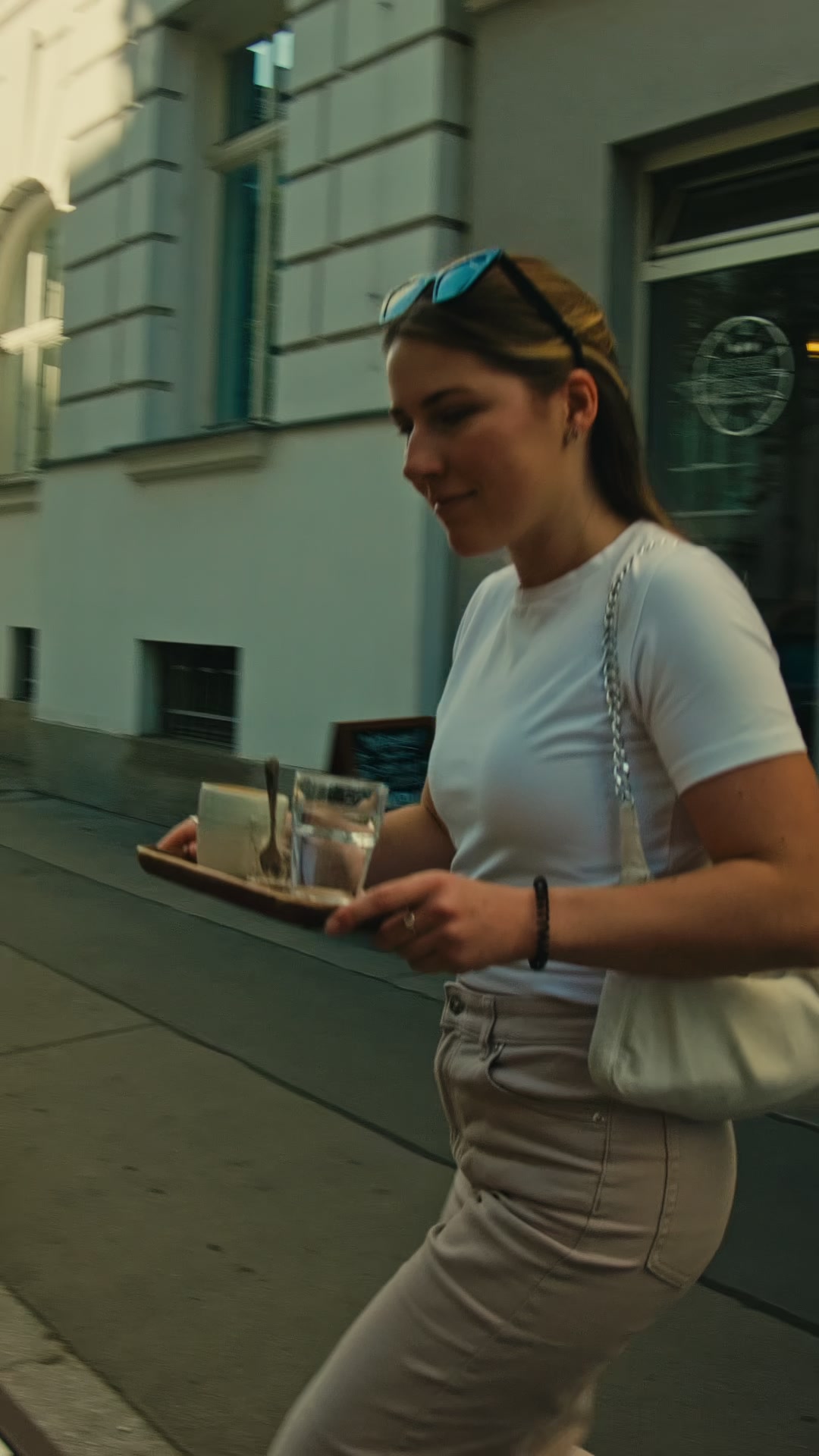 A woman carrying a tray with coffee and water outside a cafe